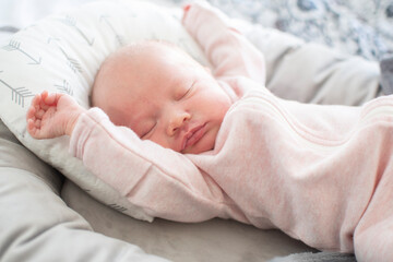 Cute caucasian baby stretching in her sleep. Sleeping newborn baby in a pink bodysuit