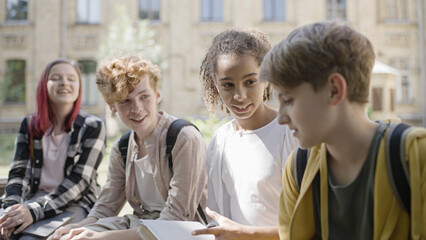 Cheerful classmates hanging out together after lessons, talking and laughing