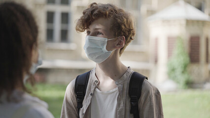 School boy and girl in medical face masks communicating after classes, epidemic