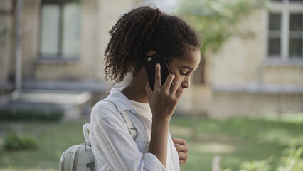 Scared biracial teen girl talking on phone, standing alone in street, calling for help