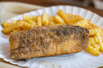 Fried cod with french fries on white plate.