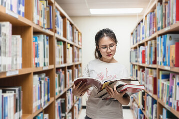 Asian woman reading and choosing a book between the bookshelves in the library.