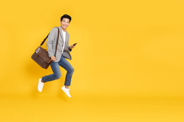 Attractive young Asian businessman jumping and typing smartphone isolated on yellow background