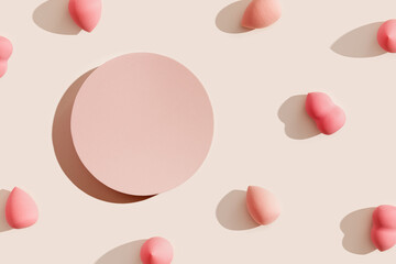 Pink makeup sponges around round platform on beige, shadow at sunlight. Cosmetic background for product presentation or foundation cream. Top view sponge and stand to show cosmetic products