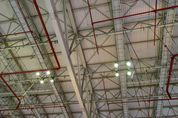 Fototapeta premium The steel construction roof of a sports hall and the spot lights on this roof. Wide shot of industrial hall empty and clean. Empty factory interior or storehouse