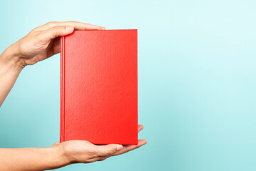 Woman hands holding book with blank red cover over light blue background. Education, back to school, self-learning, book swap, sharing, bookcrossing concept