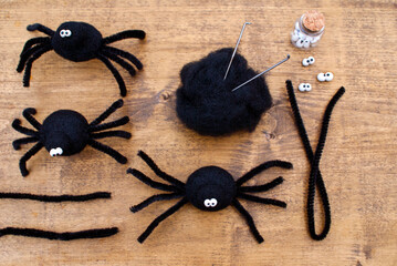 Elements for creating a felted black spider, such as: shaggy wire sticks, plastic stucco eyes, a needle and wool for felting, and the finished spiders themselves on a wooden board - Powered by Adobe