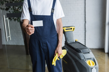 partial view of man in overalls holding empty business card near professional floor scrubber...