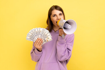 Portrait of young adult woman screaming in megaphone holding fan of dollars, announcing bonuses and...
