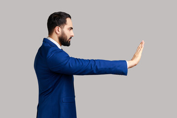 Side view of serious bearded man making stop gesture showing palm of hand, conflict prohibition...