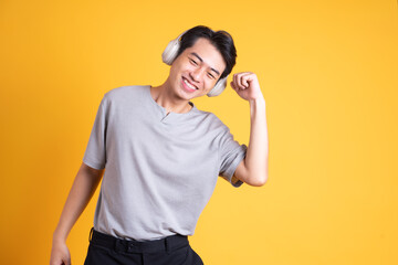 image of asian man listening to music with headphones, isolated on yellow background