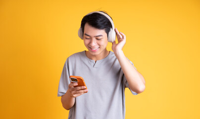 image of asian man listening to music with headphones, isolated on yellow background