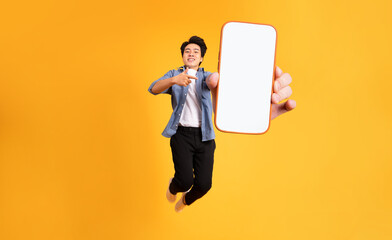 image of jumping up asian man holding smartphone in hand, isolated on yellow background