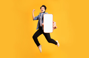 image of jumping up asian man holding smartphone in hand, isolated on yellow background