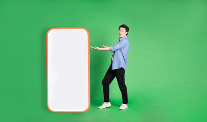 full body image of asian man standing next to big smartphone, isolated on blue background