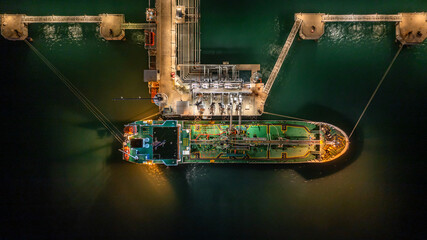 Aerial top view oil tanker ship at terminal industrial port at night for transfer crude oil to oil refinery, Business import export oil and gas petrochemical.
