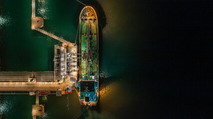 Aerial top view oil tanker ship at terminal industrial port at night for transfer crude oil to oil...
