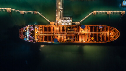 Aerial top view oil tanker ship at terminal industrial port at night for transfer crude oil to oil...