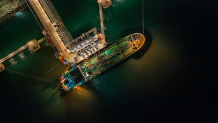 Aerial top view oil tanker ship at terminal industrial port at night for transfer crude oil to oil...