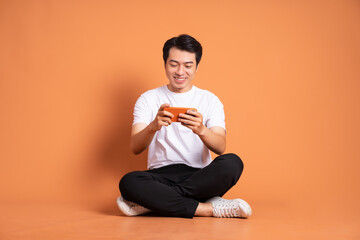 image of asian man sitting using phone and isolated on orange background