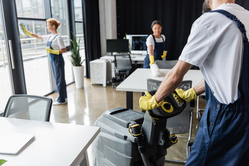 man with floor scrubber machine near multiethnic women washing windows and furniture.