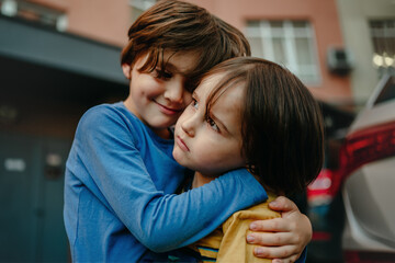 Two boys, two brothers are standing on the street and hugging tightly, the older brother takes care