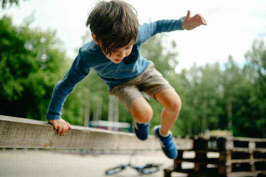A five-year-old boy parkours in the park in the summer, the child jumps over a high barrier