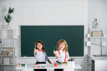 Kids creative education. Funny pupils draws in classroom on school blackboard background. School friends kids boy and girl painting together in class.