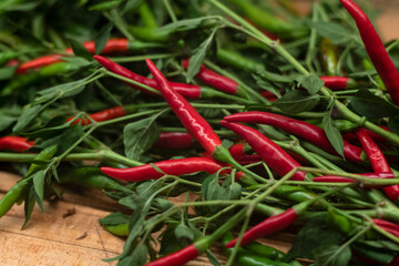 red hot chili Thai peppers with green leaves and branches on wooden cutting board