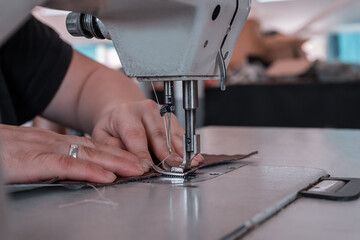 The seamstress sews at the sewing machine, threads the fabric. Women's hands