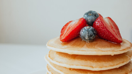 Pancakes with maple syrup, strawberry, and blueberries in a plate close-up. Sweet tasty breakfast,...