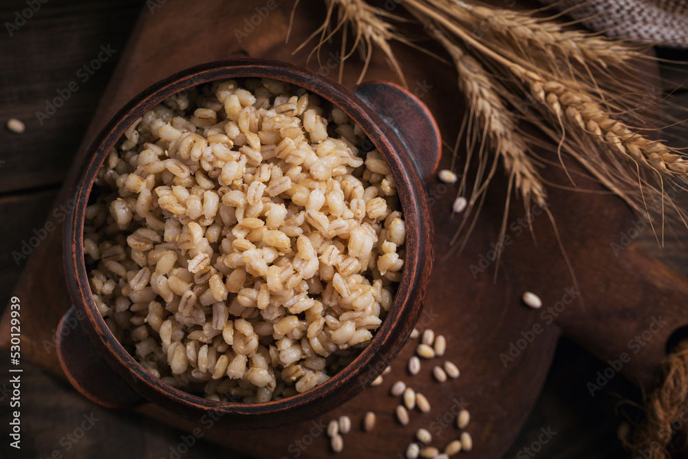 Canvas Prints Bowl of cooked peeled barley grains porridge with ears of wheat on dark wooden background. Cooking Healthy and diet food concept.