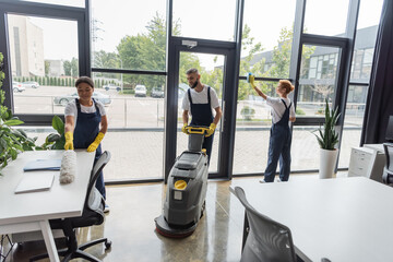 man with floor scrubber machine near interracial women washing windows and furniture.