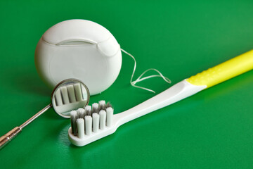 Dental mirror, dental floss and toothbrush on a green background. Dental care.