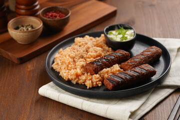 Traditional south european skinless sausages cevapcici made of ground meat and spices on black plate on dark wooden board, vegan substitute made of soy protein, with rice and sour cream