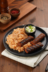 Traditional south european skinless sausages cevapcici made of ground meat and spices on black plate on dark wooden board, vegan substitute made of soy protein, with rice and sour cream