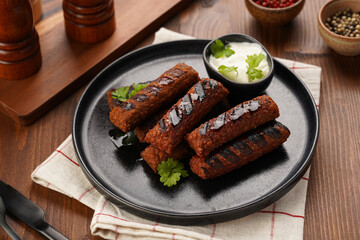 Traditional south european skinless sausages cevapcici made of ground meat and spices on black plate on dark wooden board, vegan substitute made of soy protein, with rice and sour cream