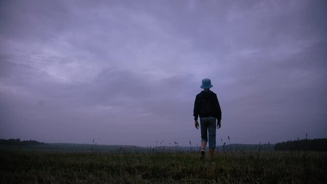 teen boy walks on a field in rainy weather in the evening, evening walk against the backdrop of beautiful clouds
