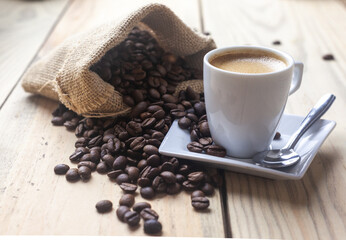 Taza de café sobre un platillo junto a un saco con granos de cafe