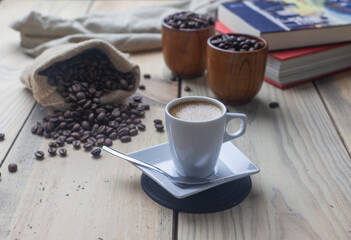 Taza de café caliente junto a algunos libro y granos de café tostado