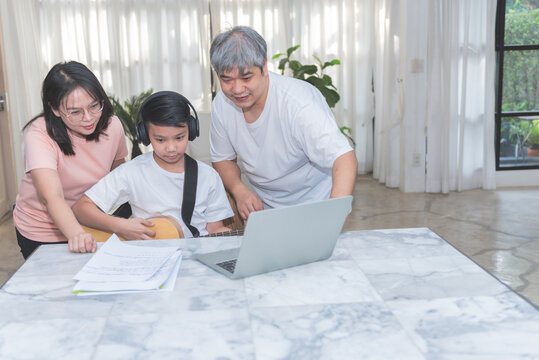 Asian Teenage Boy Studying Music, Playing Guitar Online At Home, With A Father And Mother To Take Care Of And Help In Learning, To Asian Family And Education Online Concept.