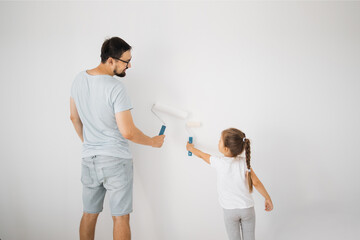 Fototapeta premium Repair in the apartment. Back view of happy family of father and little cute child daughter paints the wall with white paint.