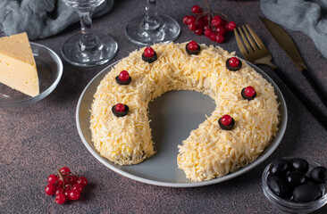 Festive salad in shape of horseshoe with chicken, eggs, cheese and olives on brown table