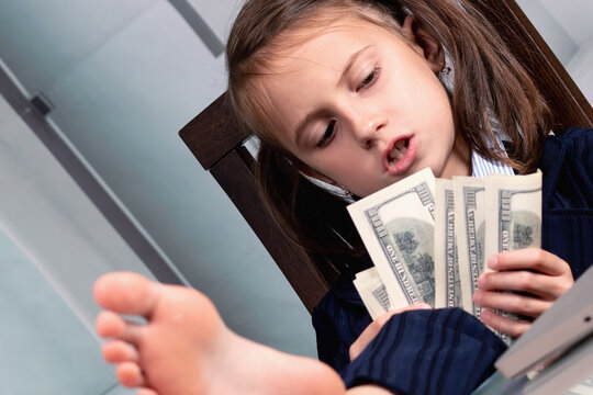 Close up humorous portrait of happy cute young business girl counts US Dollar money with bare feet on the table. Horizontal image.