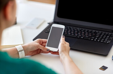 business, technology and people concept - close up of woman with smartphone and laptop computer working at home office