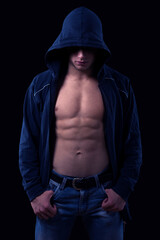 Obraz na płótnie Canvas Young muscular man wearing hoodie sweater and jeans standing against black background