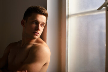 Young muscular man standing in front of room window