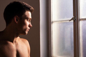 Fototapeta na wymiar Young muscular man standing in front of room window