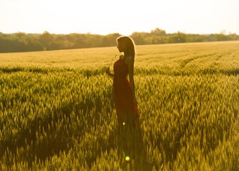 Pretty long haired slim woman in long dress enjoys the sunset next to a meadow, and holds a piece...