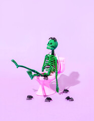 Green skeleton on pink toilet bowl with spiders. A creative, festive idea for Halloween. Funny idea...
